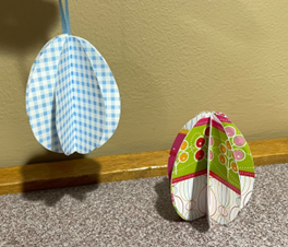 Two 3-D paper eggs, one with a white and blue plaid pattern and the other with a floral wallpaper style.